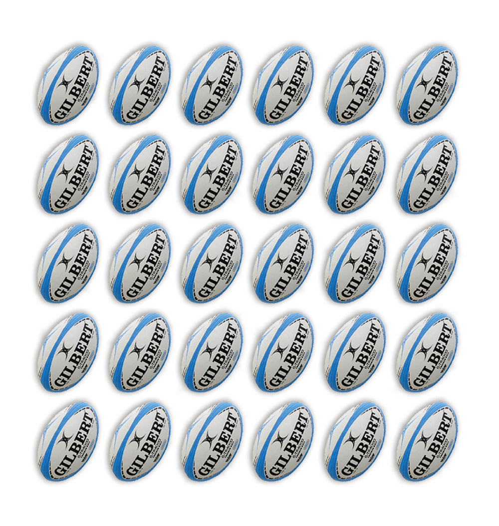 Stack of 30 Gilbert G-TR4000 trainer rugby balls in white with black and orange accents alongside two large breathable storage bags